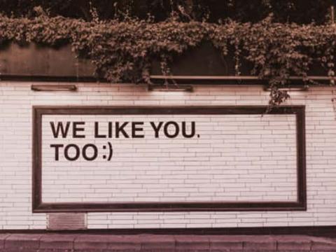 The tiled side of a building with "WE LIKE YOU. TOO :)" in big letters on it